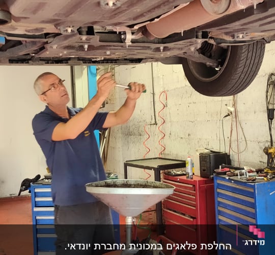 אדם מתקן רכב במוסך עם כלים וציוד